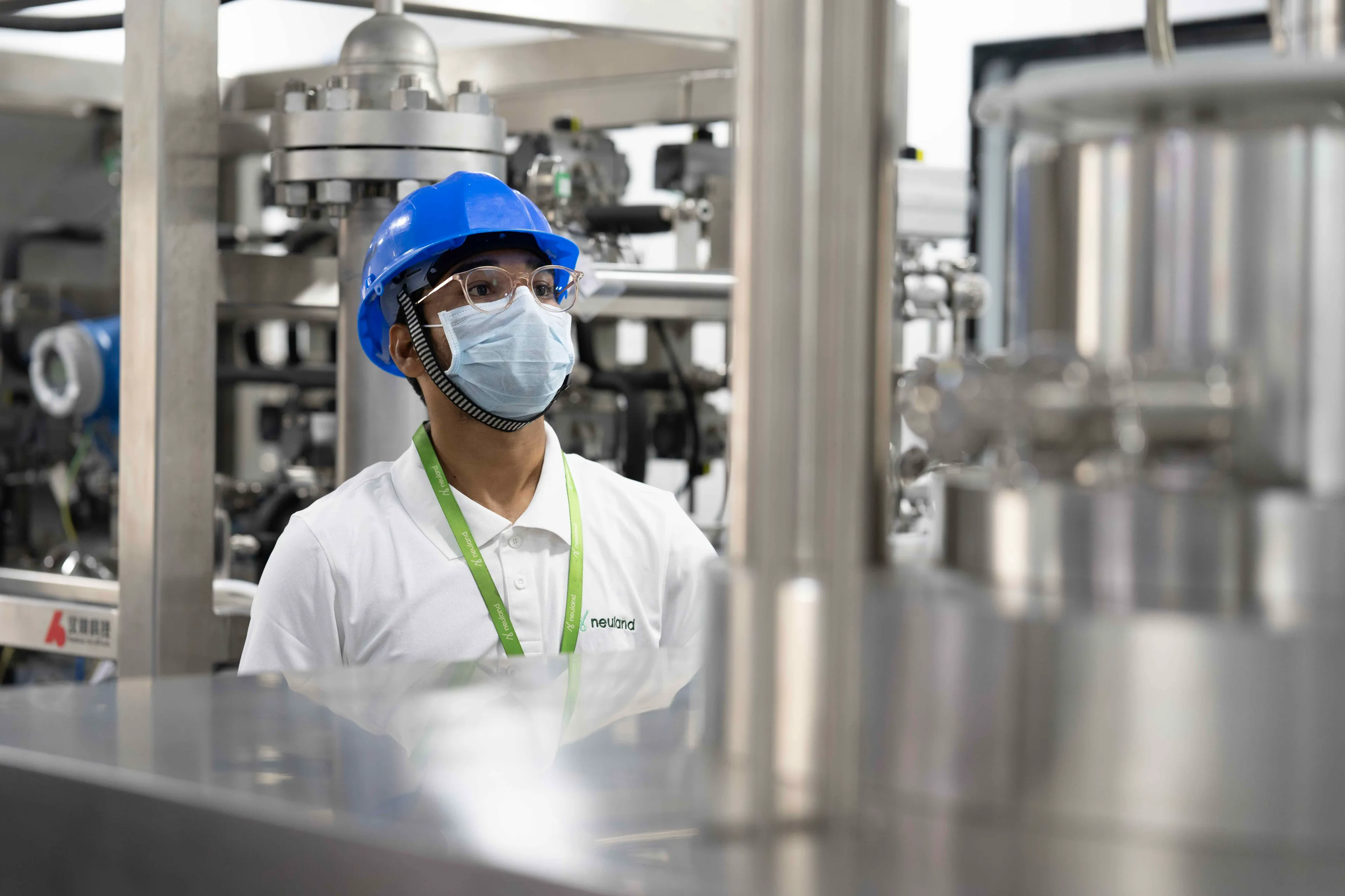 Neuland operator in a blue hard hat, safety glasses and face mask inside a cGMP API manufacturing plant